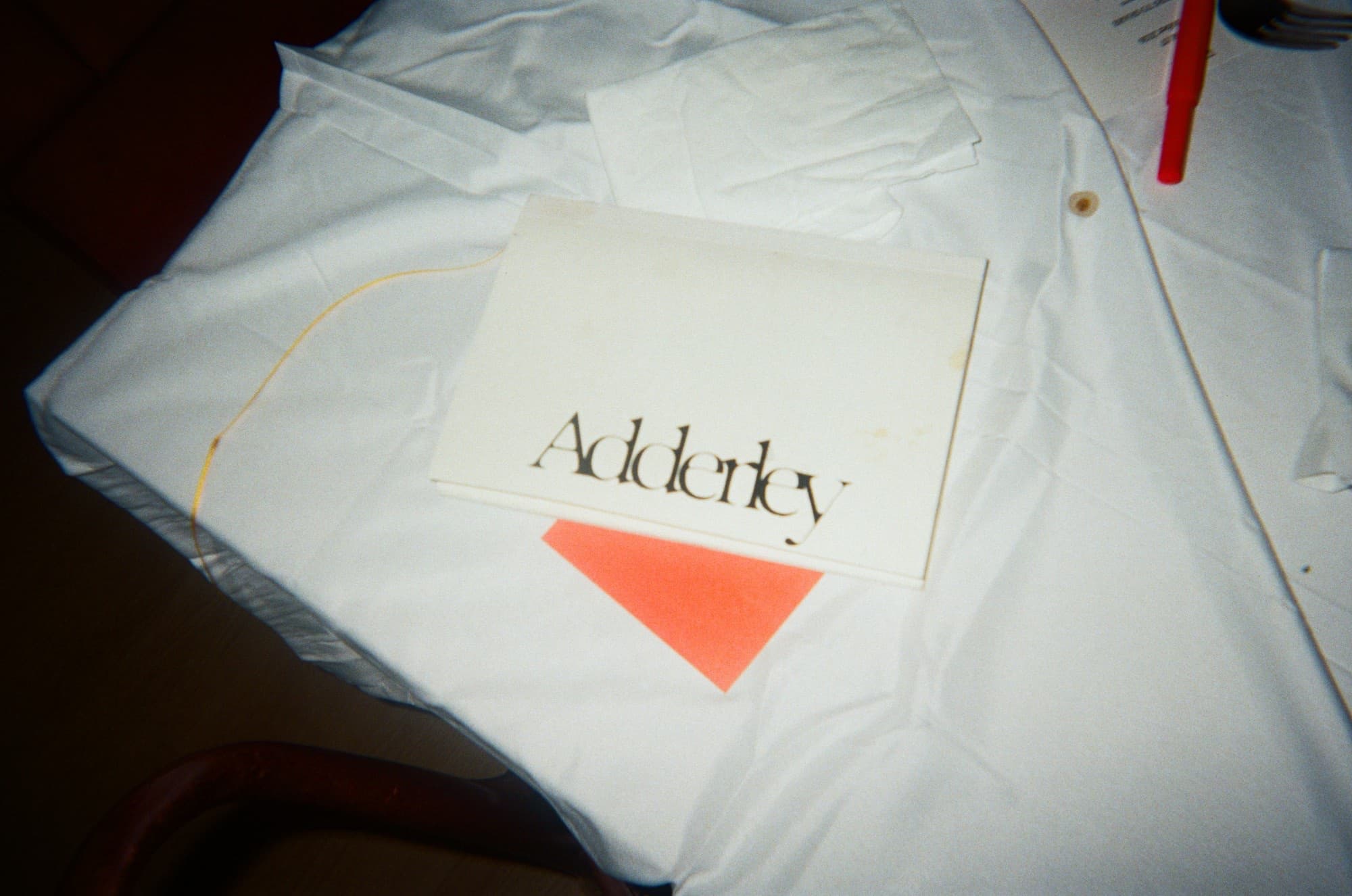 An Adderley card on a crumpled white tablecloth at the end of a dinner, a cinnabar napkin beneath it
