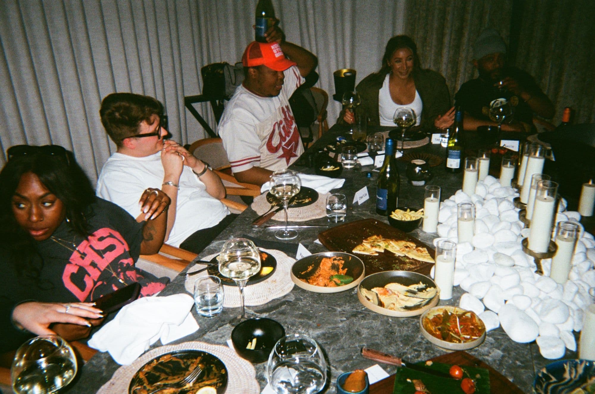 Guests along a long stone table at the second Manchester room, plates passed between candles and white pebbles